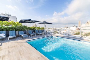 A rooftop pool area with lounge chairs and umbrellas, surrounded by greenery and city views. - Oceanfront Oasis: 2-BR Apartment on Ocean Drive (Miami Beach)