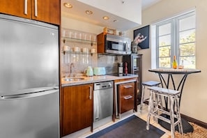 A modern kitchen with stainless steel appliances, wooden cabinets, and a small dining area with a table and stools. - Oceanfront Oasis: 2-BR Apartment on Ocean Drive (Miami Beach)