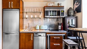 Een moderne keuken met roestvrijstalen apparatuur, houten kastjes, een glazen plank met kopjes, een magnetron en een Boeddhabeeld.