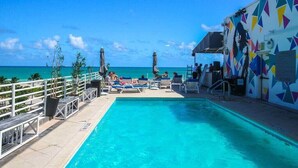 A pool area with lounge chairs, a railing, and a view of the ocean.