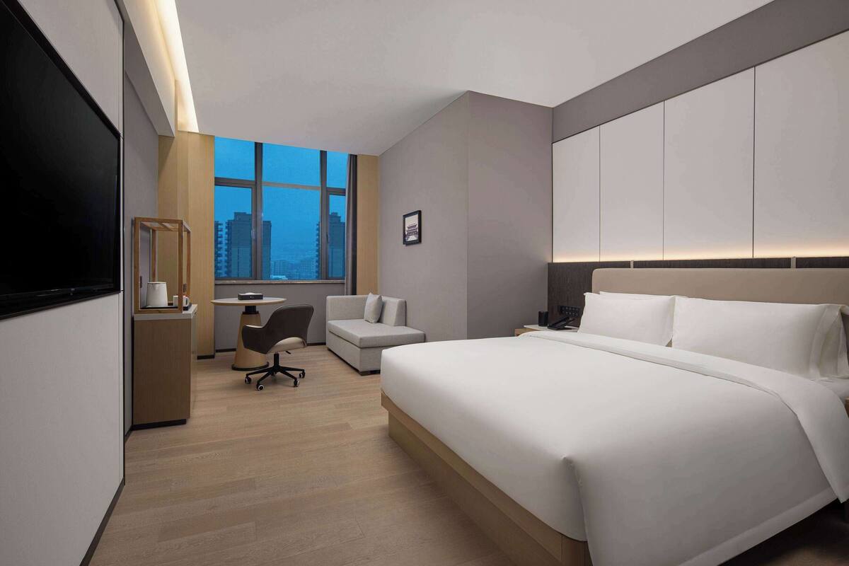 A modern hotel room with a large bed, a desk, a chair, and a TV.
