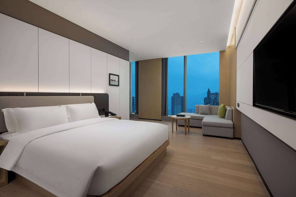 A modern hotel room with a large bed, a sofa, a small table, and a TV.