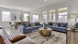A spacious living room with a large sofa, a coffee table, and a dining area with chairs and a table.