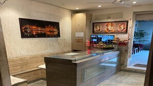 A modern bathroom with a glass partition, a sink, and a mirror. There is a framed picture on the wall and a ceiling fan. - Hotel Pace Hero Honda Chowk (Gurugram)