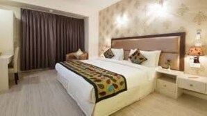 A hotel room with a large bed, a bedside table, a nightstand, a lamp, and a curtain. - Hotel Pace Hero Honda Chowk (Gurugram)