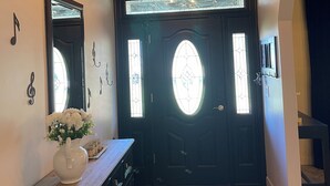 A foyer with a wooden ceiling, a black door with stained glass windows, a mirror, and a white vase with flowers on a wooden dresser. - V&V Resort (Greensboro)