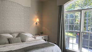 A bedroom with a large bed, a nightstand, a lamp, and a view of the outdoors through a window. - V&V Resort (Greensboro)