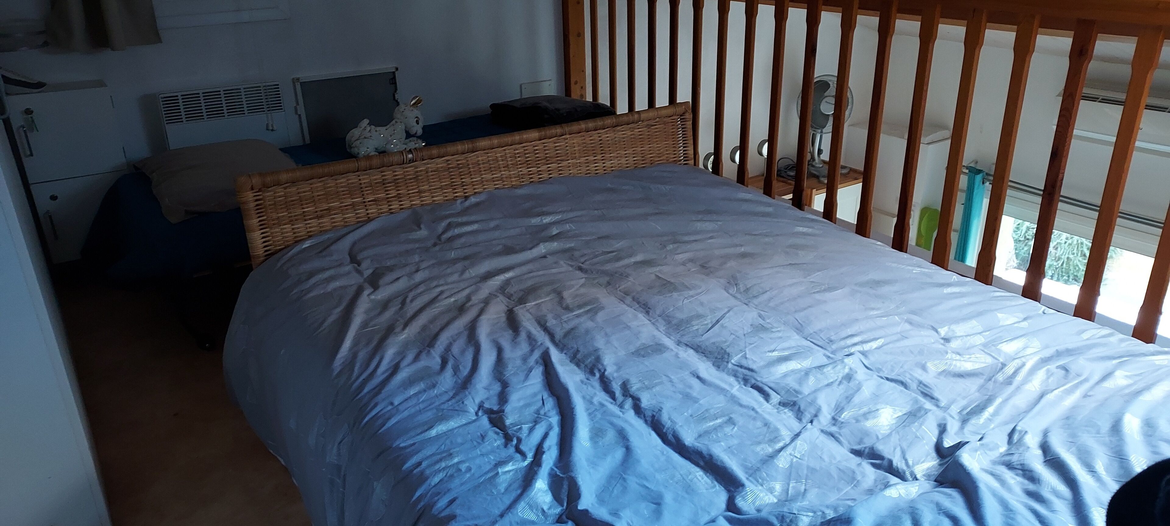 A bedroom with a bed, a wicker headboard, a small table with a lamp, and a window with a view.