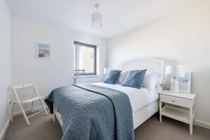 A bedroom with a bed, bedside tables, a window, and a white radiator. - Modern Home with Sea Views, Newquay (Newquay)