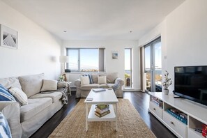 A modern living room with a sofa, coffee table, TV, and large windows.