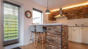 Une cuisine moderne avec un mur d’accent en pierre, un plancher en bois et un coin bar équipé de deux tabourets.