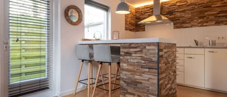 A modern kitchen with a stone accent wall, wooden flooring, and a bar area with two stools.