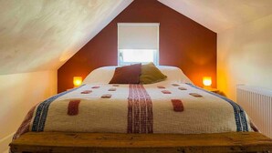 Een gezellig slaapkamer op zolder, met een schuine hemel, een groot bed met een geborduurd sprei, twee bedlampen en een raam met uitzicht.