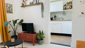 Een moderne woonkamer met een televisie, bank en eettafel, die uitkomt op een keuken met witte kasten en een betegelde achterwand.