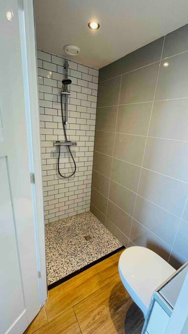 Un baño pequeño con ducha, inodoro y suelo de baldosas.
