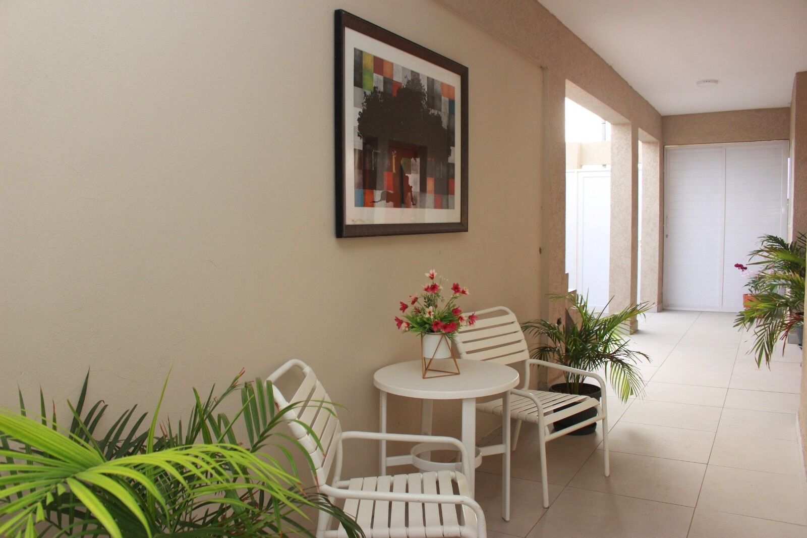 Un pasillo con una silla blanca, una mesita redonda con un florero y un cuadro en la pared.