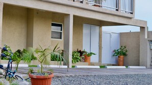 Un bâtiment moderne à deux étages, doté d’un toit plat, de grandes fenêtres et d’un balcon. On y trouve des plantes en pot et un vélo garé devant.
