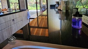 A modern kitchen with a black countertop, wooden cabinets, and a view of a garden through large windows.