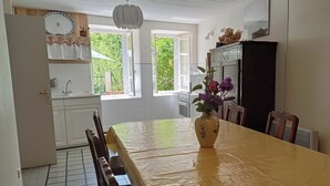 Ett kök med ett matbord, stolar, en vas med blommor och ett kylskåp.