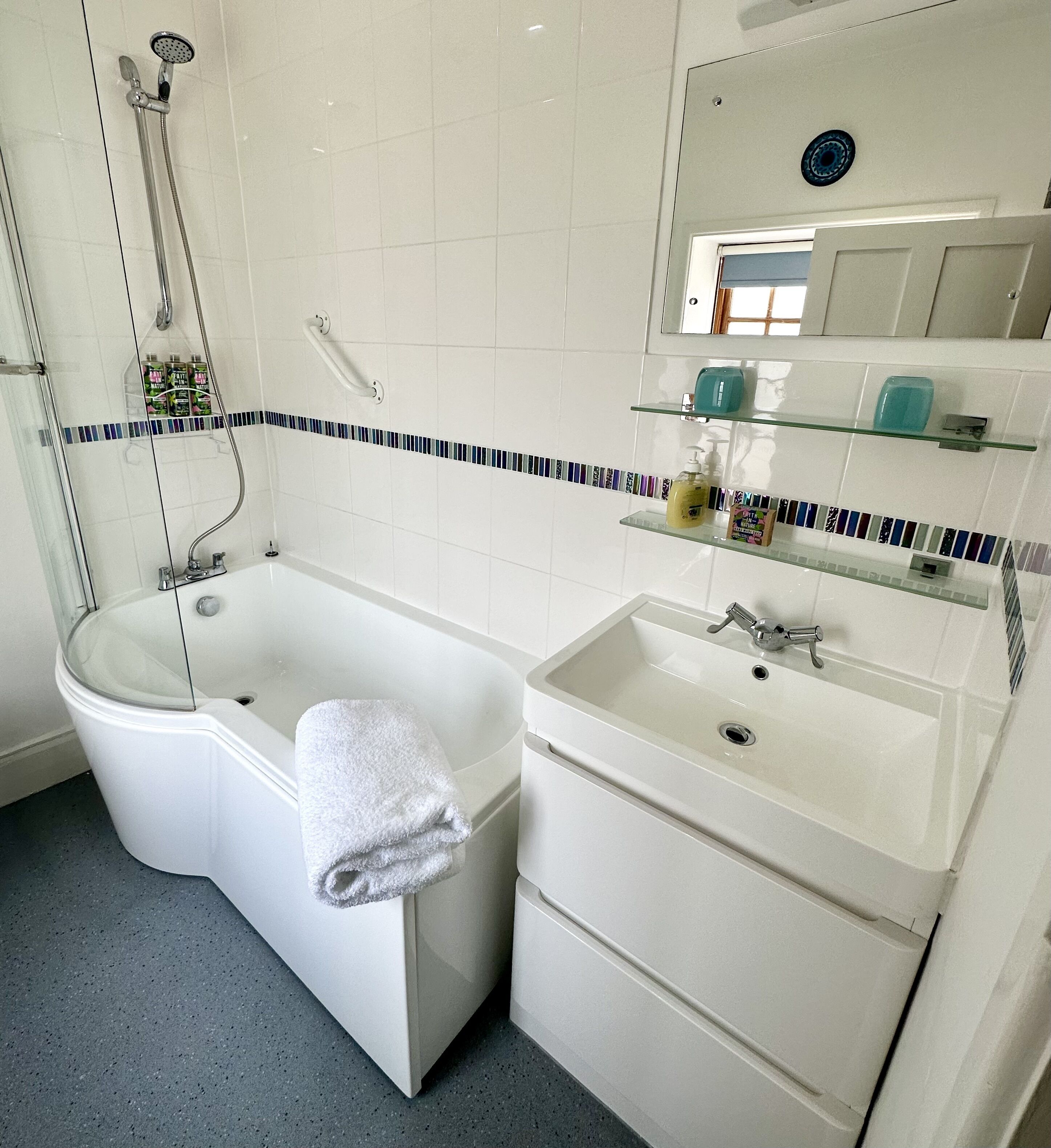 A bathroom with a bathtub, a sink, and a shower. There are toiletries on the shelves.