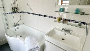 A bathroom with a bathtub, a sink, and a shower. There are toiletries on the shelves.