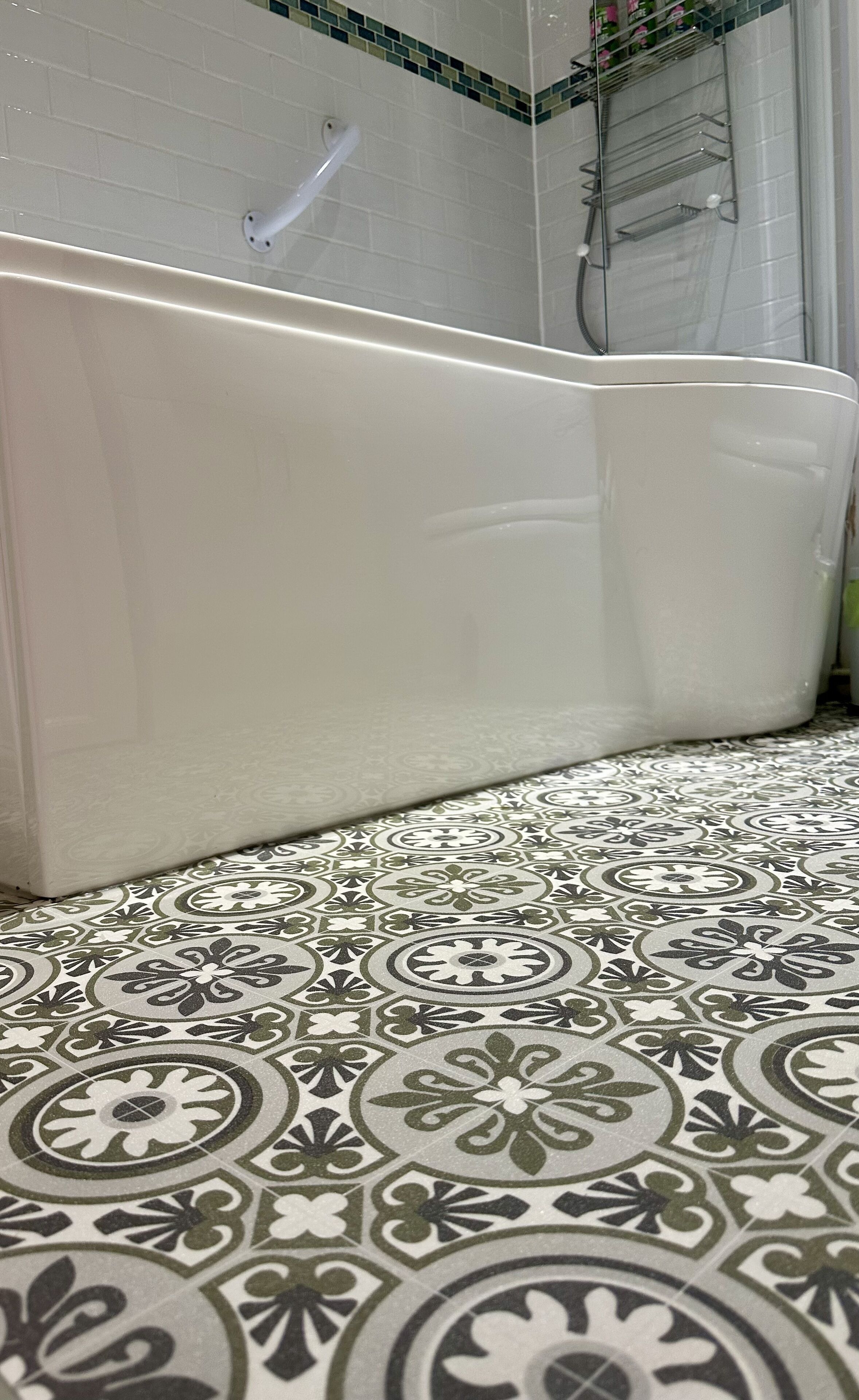 A bathroom with a white bathtub, patterned floor tiles, and a shower area with a glass door.
