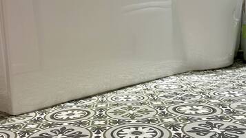A bathroom with a white bathtub, patterned floor tiles, and a shower area with a glass door.
