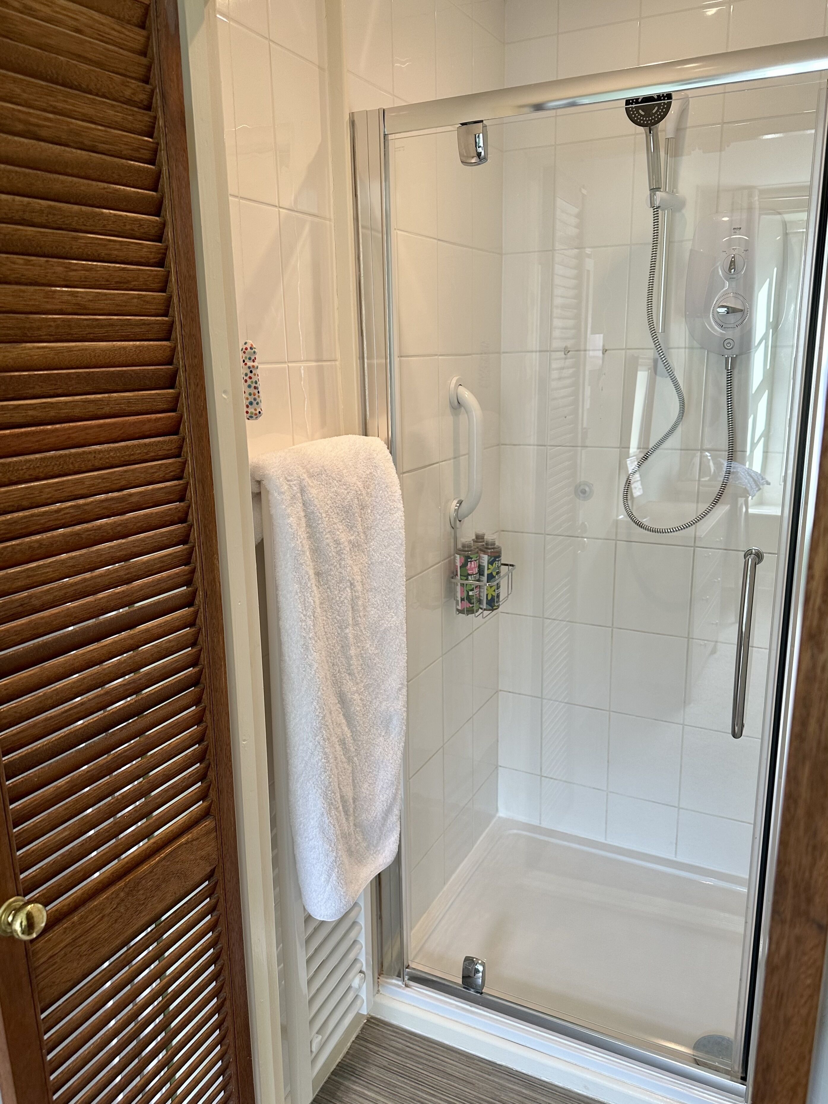 A glass-enclosed shower with a handheld showerhead and a handheld shower attachment.