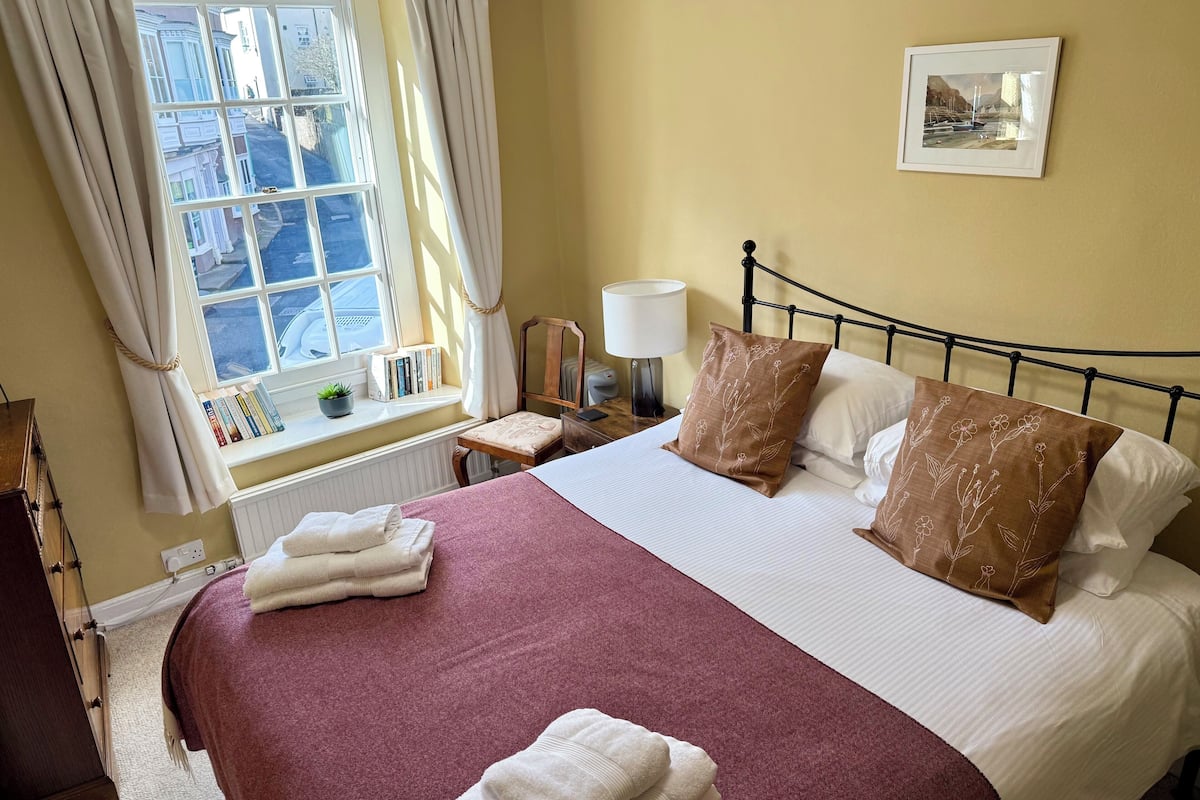 A neatly made bed with a red bedspread, two pillows with floral patterns, and a bedside table with a lamp.