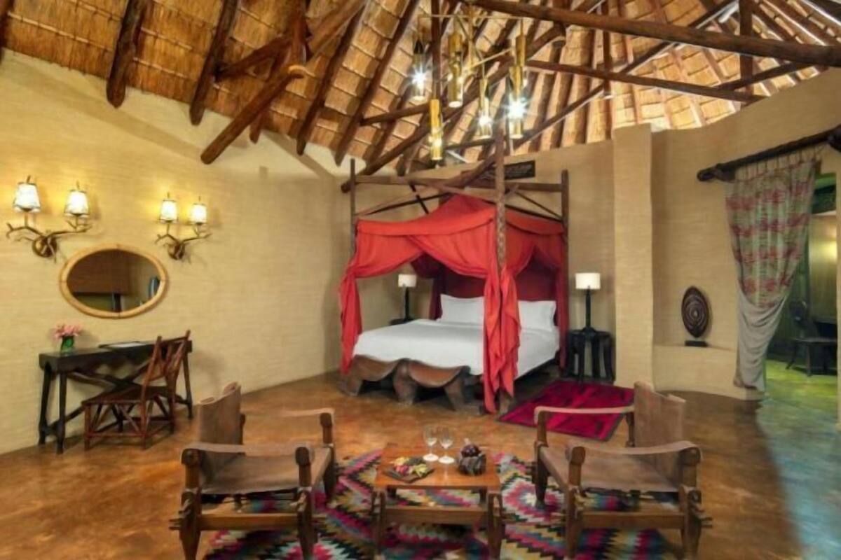 Una habitación con una cama bajo un dosel rojo, un espejo redondo, un escritorio de madera y una silla.