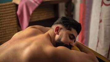A person lying on a bed in a room with a wicker chair and a pink cloth in the background.