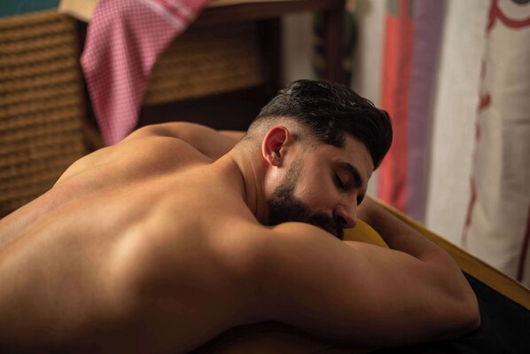 A person lying on a bed in a room with a wicker chair and a pink cloth in the background.