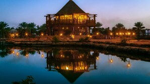 A large, multi-story building with a pyramid-shaped roof, surrounded by palm trees and a calm body of water reflecting the structure.