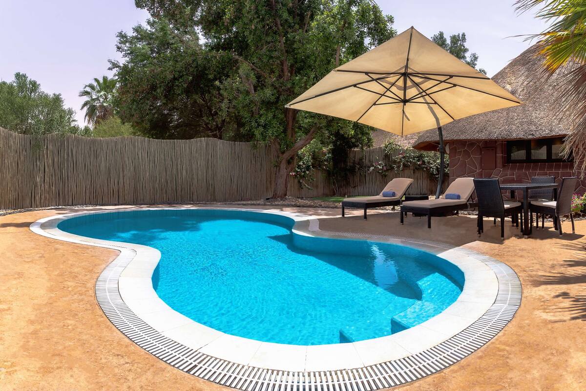 Una piscina con borde curvo, rodeada de sillas de descanso y una sombrilla.