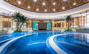 An indoor swimming pool with a modern design, surrounded by palm trees and a large mural of giraffes.