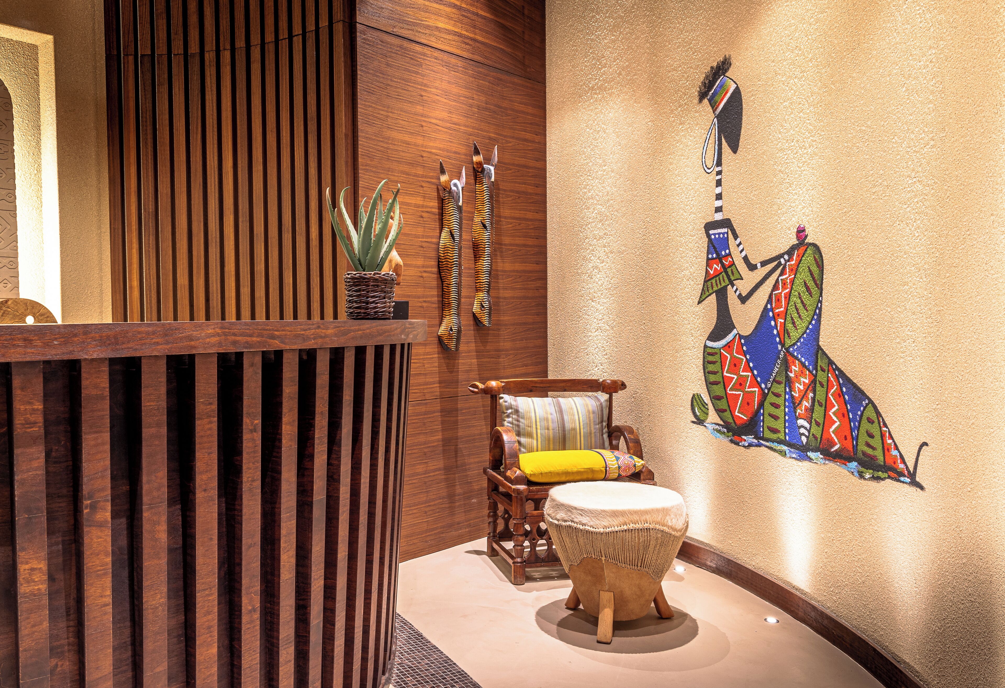 A reception area with a wooden reception desk, a cushioned chair, a small round table, and a wall mural.