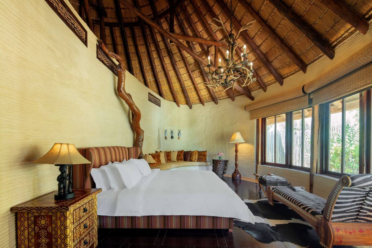 Un dormitorio amplio con una cama grande, un cabecero de madera, una araña y vistas al exterior a través de amplios ventanales.