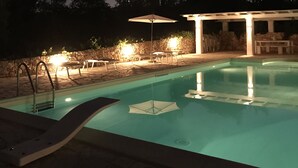 A swimming pool with a stone deck, a covered seating area, and a stone wall in the background. - TRULLO SUITE 'THE QUEEN' in Itria Valley with swimming pool (Martina Franca)