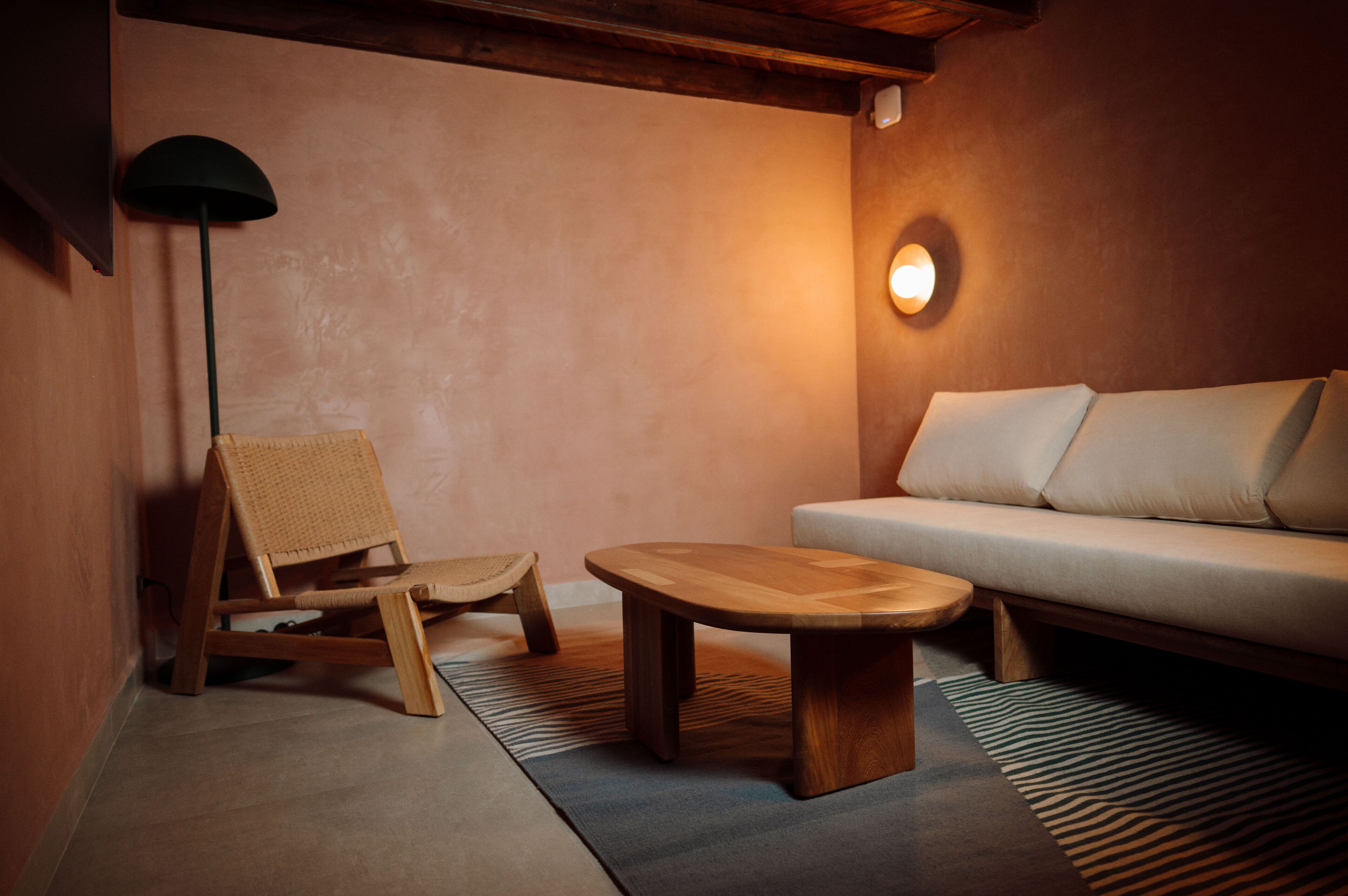 Una habitación acogedora con una silla de madera, una mesita redonda y un sofá.