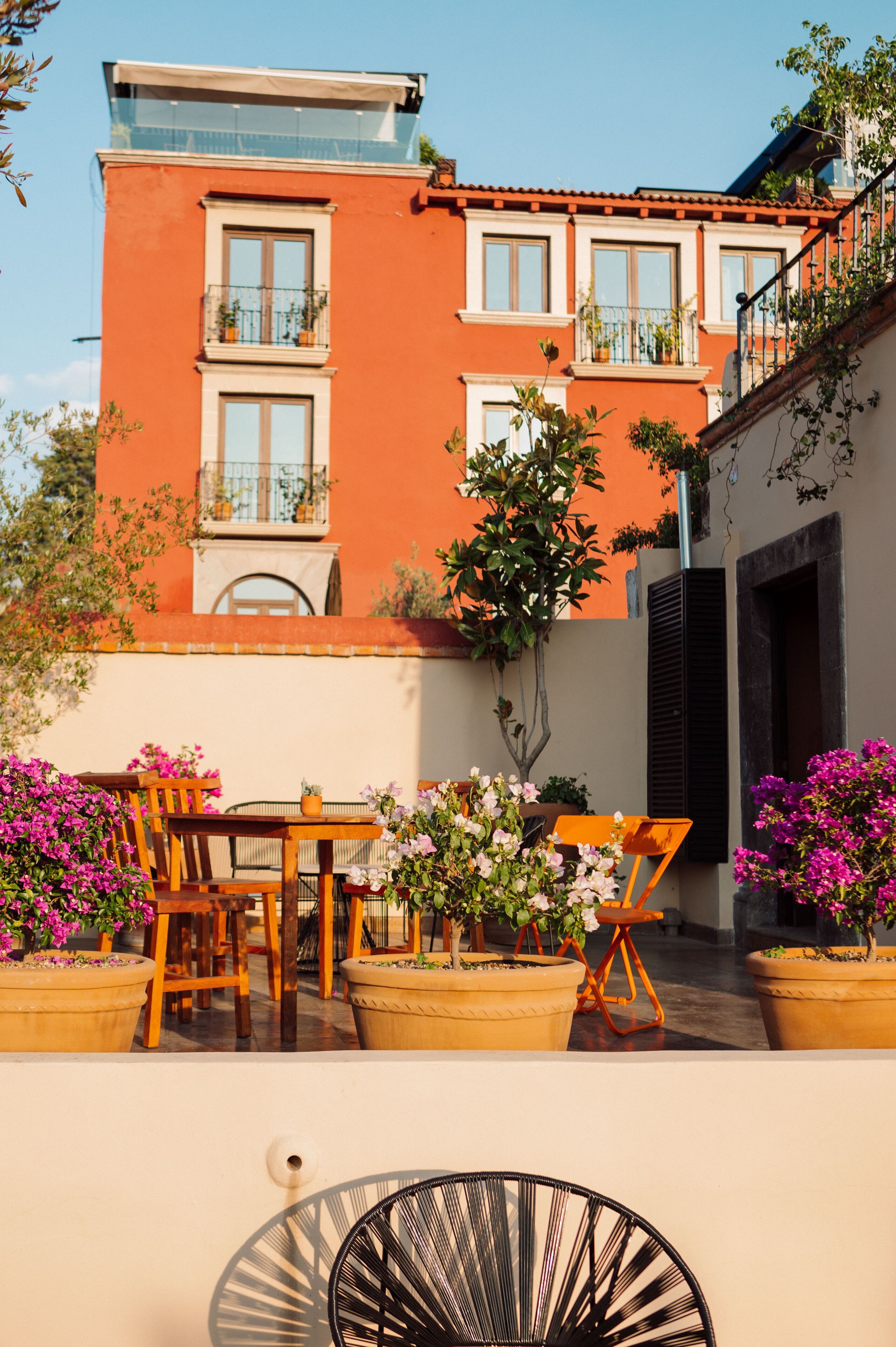 A building with a red facade, balconies with potted plants, and a patio area with wooden furniture and flower pots.