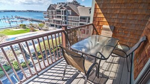 Un balcon avec une table en verre et une chaise en osier, donnant sur une marina et des immeubles.