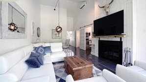 A spacious living room with a white sofa set, a wooden coffee table, and a large flat-screen TV mounted above a fireplace. - Croissant des Soleils - RVMT (Mont-Tremblant)