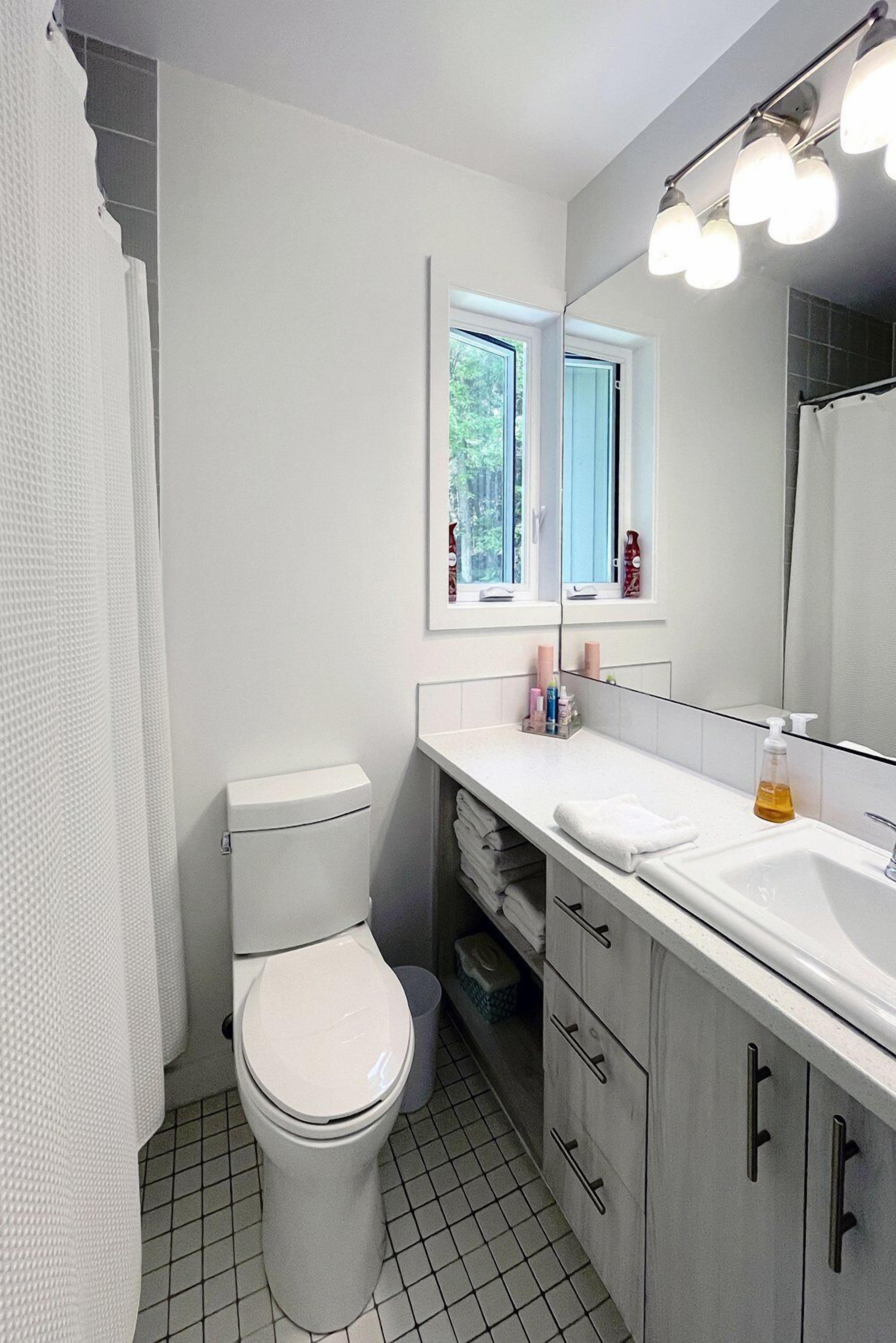 Ein Badezimmer mit Toilette, Waschbecken, Spiegel und Fenster.