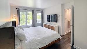 A modern bedroom with a large bed, a TV on a stand, and a view of the outdoors through the windows. - Croissant des Soleils - RVMT (Mont-Tremblant)