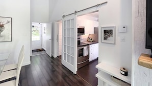 A modern kitchen with white cabinets, stainless steel appliances, and a sliding glass door leading to a dining area. - Croissant des Soleils - RVMT (Mont-Tremblant)