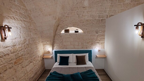 Ein gemütliches Zimmer mit Steinwand, einem Bett mit türkisfarbenem Bettzeug und zwei Wandleuchten.