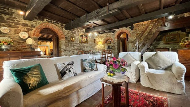 A rustic interior with a stone wall, wooden beams, a sofa, armchairs, and a small table with a vase of flowers. - Villa in Sant'angiolo with 5 bedrooms sleeps 12 (Sant'angiolo)