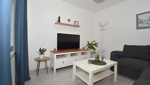 A modern living room with a flat-screen TV, a sofa, a coffee table, and decorative plants. - Charming 5-bed House in City Center and Car Park (Birmingham)
