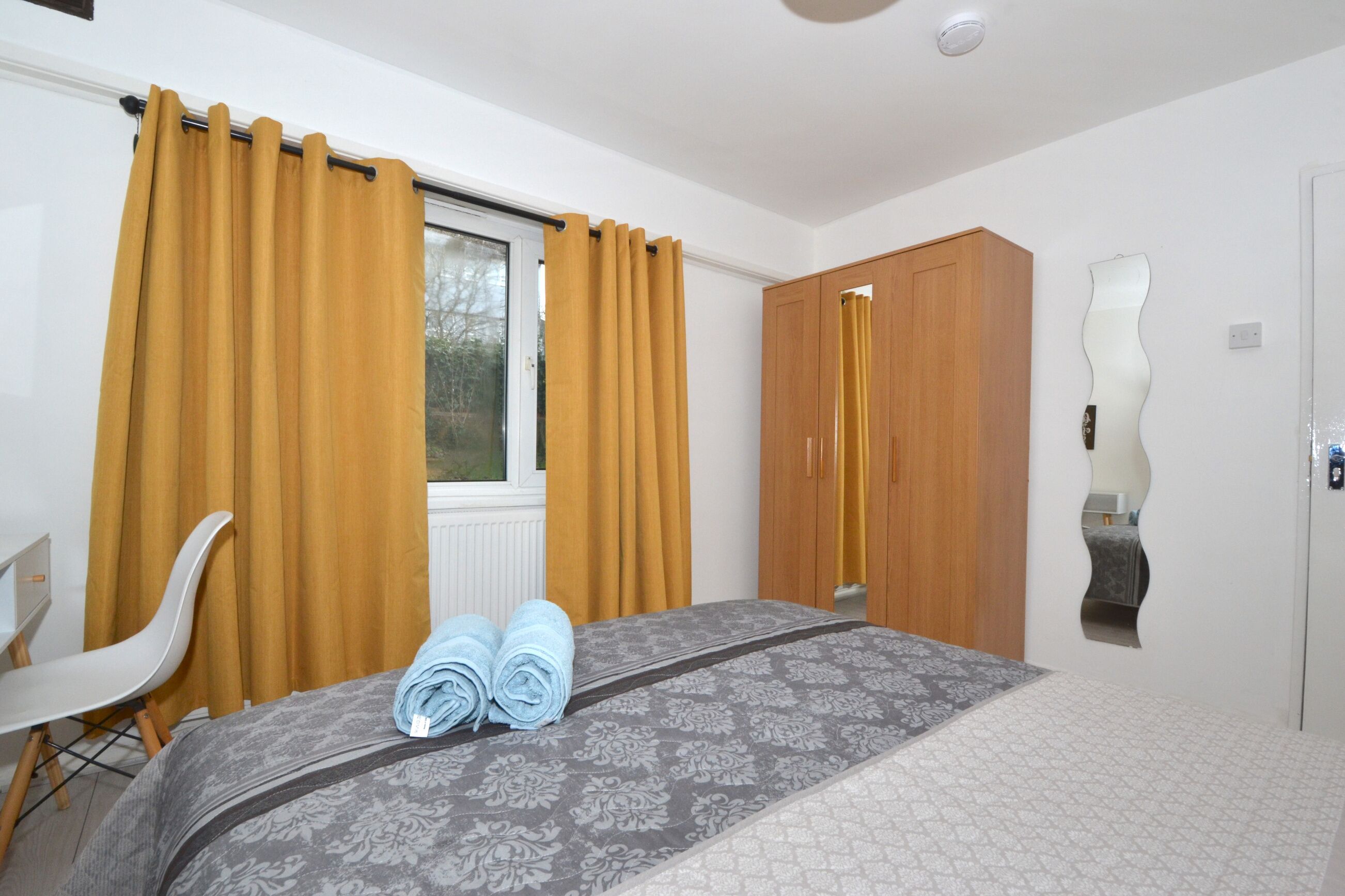 A bedroom with a bed, a chair, a wardrobe, and a window with curtains.