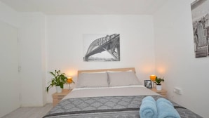 A bedroom with a bed, two bedside tables, a nightstand, a wall-mounted picture of a bridge, and two potted plants. - Charming 5-bed House in City Center and Car Park (Birmingham)